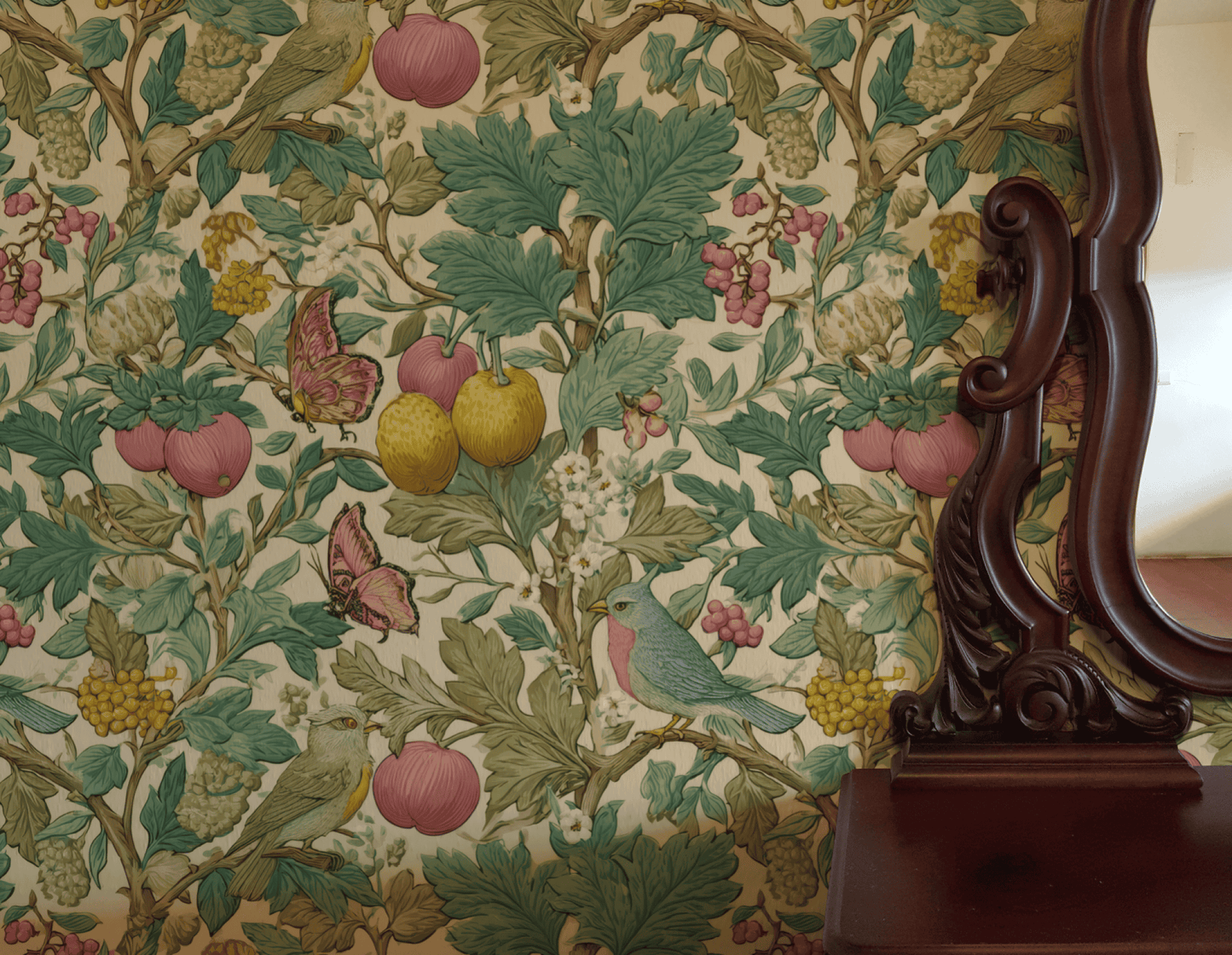 An ornate wooden mirror sits beside a wall adorned with Eden Symphony Wallpaper, featuring green leaves, yellow fruit, pink flowers, birds, and butterflies.