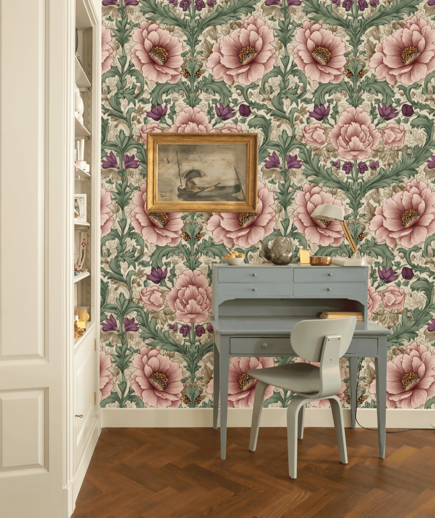 A small gray desk and chair sit against a wall covered in Botanical Harmony Wallpaper, beneath a framed painting; wooden floor and built-in shelves are visible.