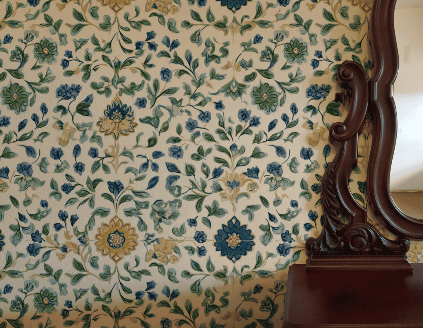 Bloom Haven Wallpaper in soft greens and blues creates a serene atmosphere, complemented by a dark wooden mirror and the edge of a wooden table on the right.