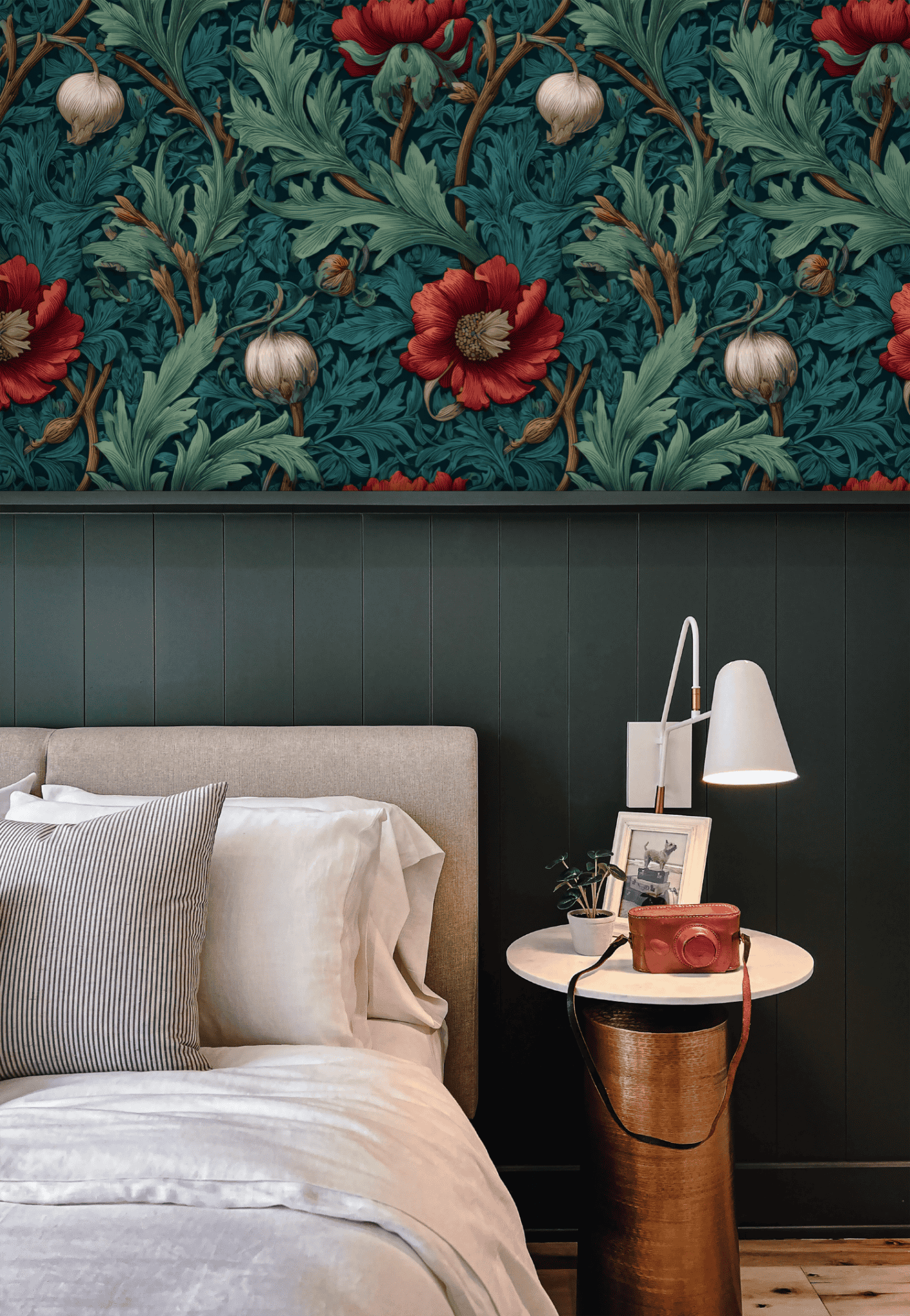 A beige bed is beside a nightstand with a lamp, framed photo, and book. The wall showcases dark green paneling and Crimson Flora Wallpaper with deep red blooms and detailed foliage for timeless elegance.