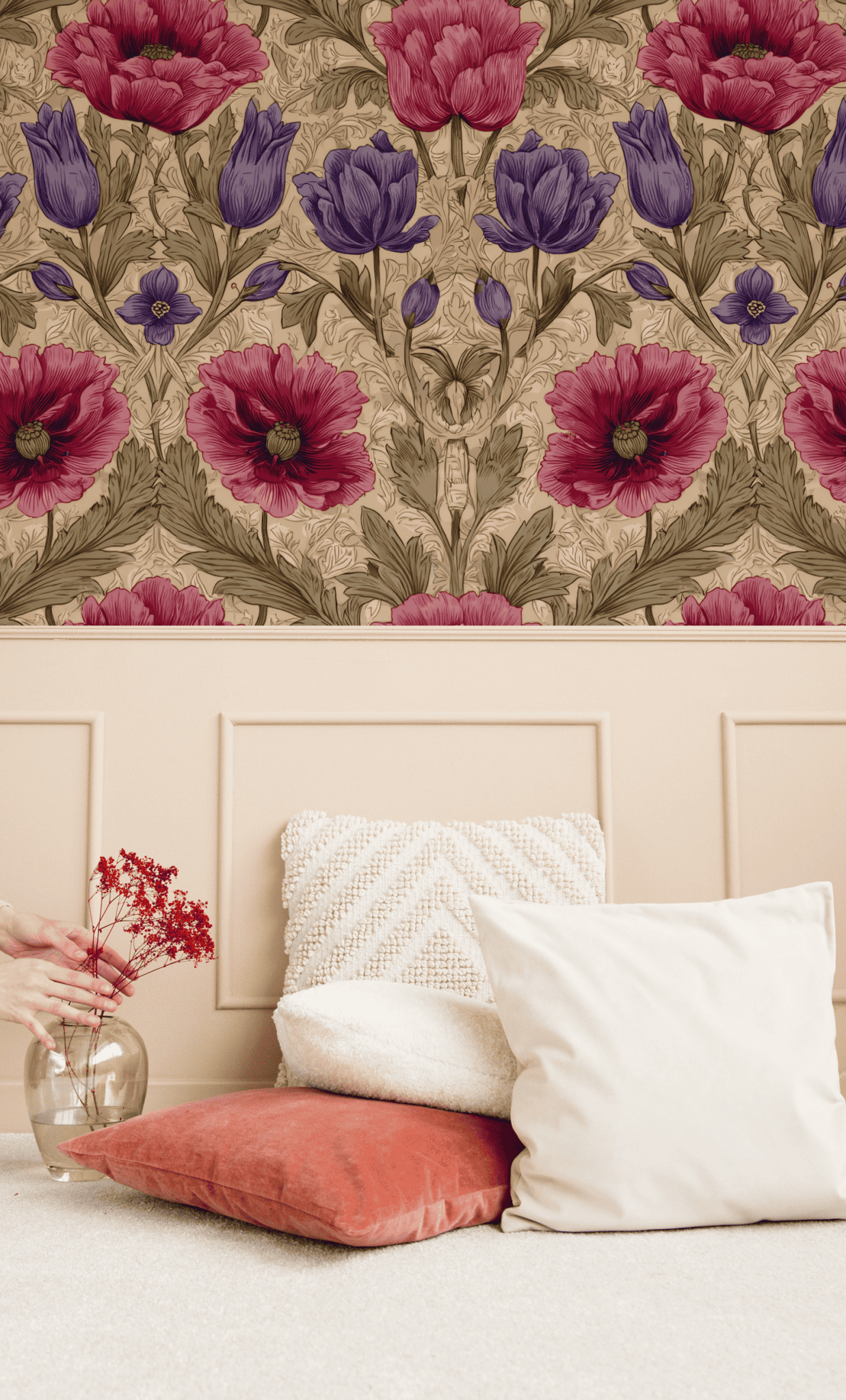 A beige wainscoted wall with Vintage Blossom Wallpaper featuring red and purple flowers brings romantic charm above a cream carpet, highlighted by white and orange cushions and a small vase of red flowers.