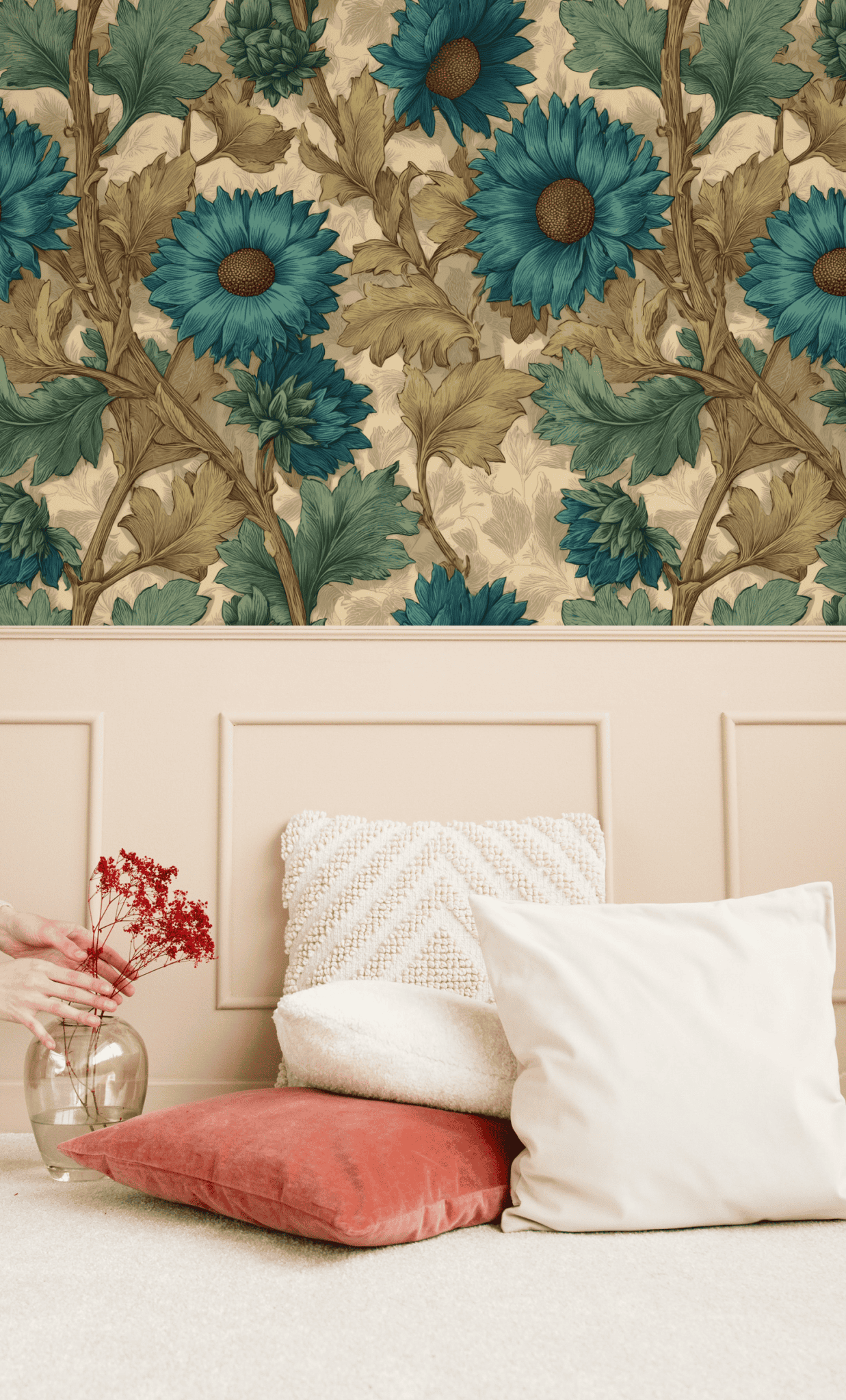 A hand sets a vase with red dried flowers on the floor by cream and rust cushions, against a paneled wall decorated with Azure Blossom Wallpaper featuring elegant azure blooms.