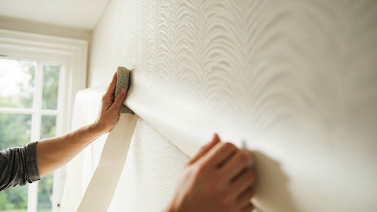 Two hands smoothing a freshly hung strip of wallpaper flat against a wall