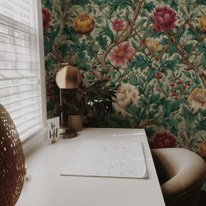 A white desk with a calendar, lamp, and chair sits by a window; the wall behind features Botanical Whimsy Wallpaper with green leaves and pink, yellow, and red flowers for a vibrant botanical garden feel.