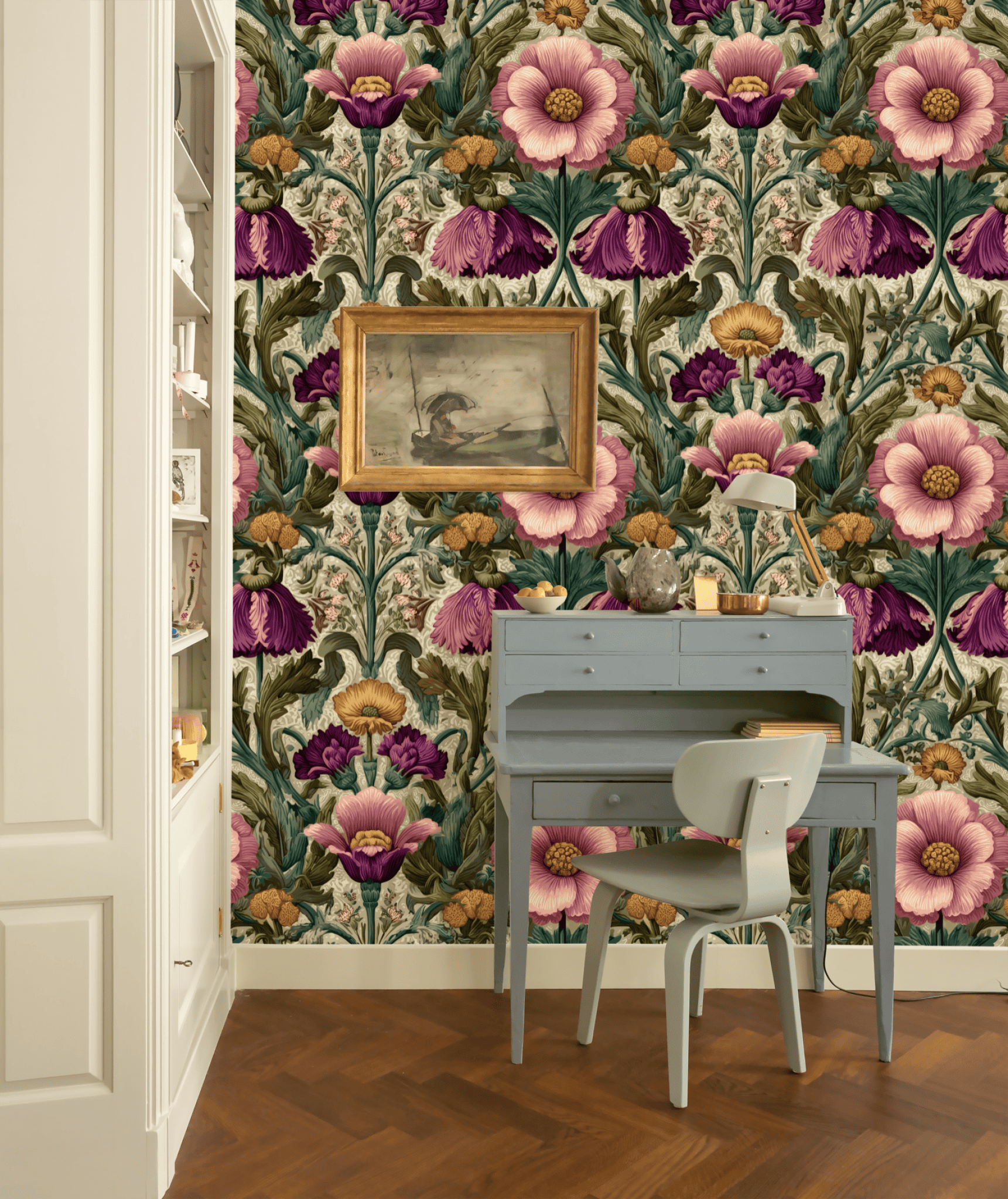 A small gray desk and chair sit against a wall of Blossom Rhapsody Wallpaper in bold pink, purple, and green florals; a framed painting and decorative items add classic elegance on and above the desk.