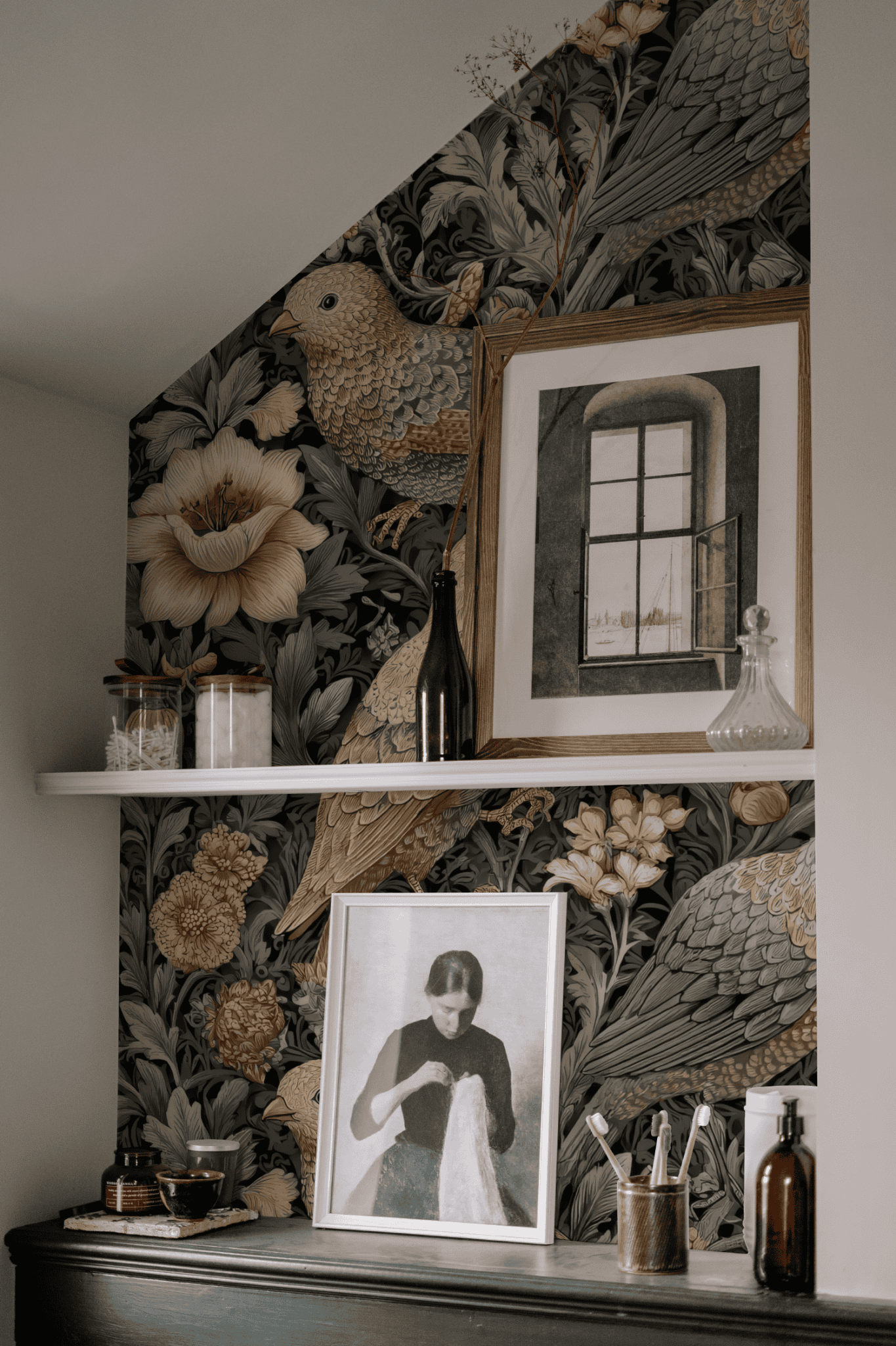 Shelf with glass jars, vases, and framed artworks stands before Garden Reverie Wallpaper, which features birds and blooms; a portrait and window art enhance the delicate charm of this elegant display.