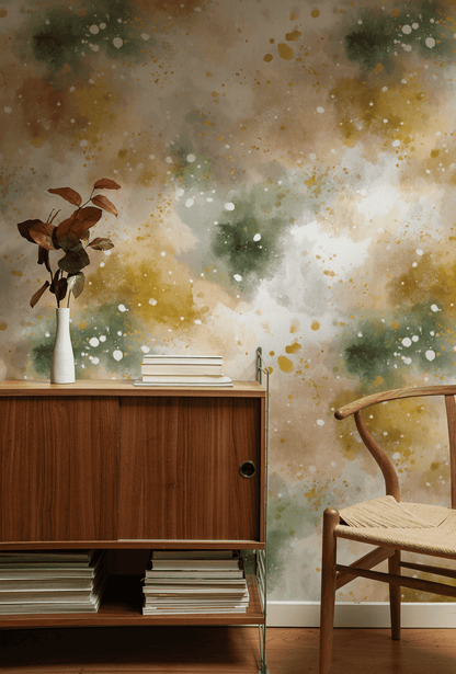 A wooden cabinet with books and a white vase of brown leaves stands against a wall decorated with Aurora Mist Wallpaper. Nearby, a wooden chair with a woven seat completes the serene setting.