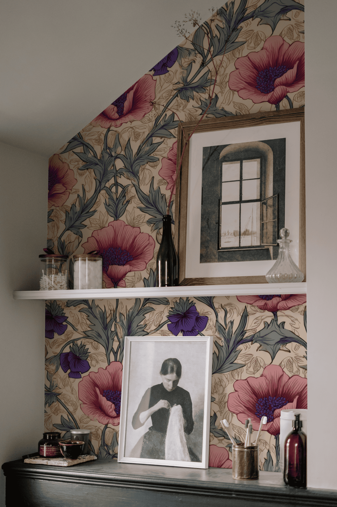 A wall adorned with Blossom Reverie Wallpaper, two white shelves displaying framed art and decorative bottles, and a black dresser with a vintage portrait together evoke timeless elegance.