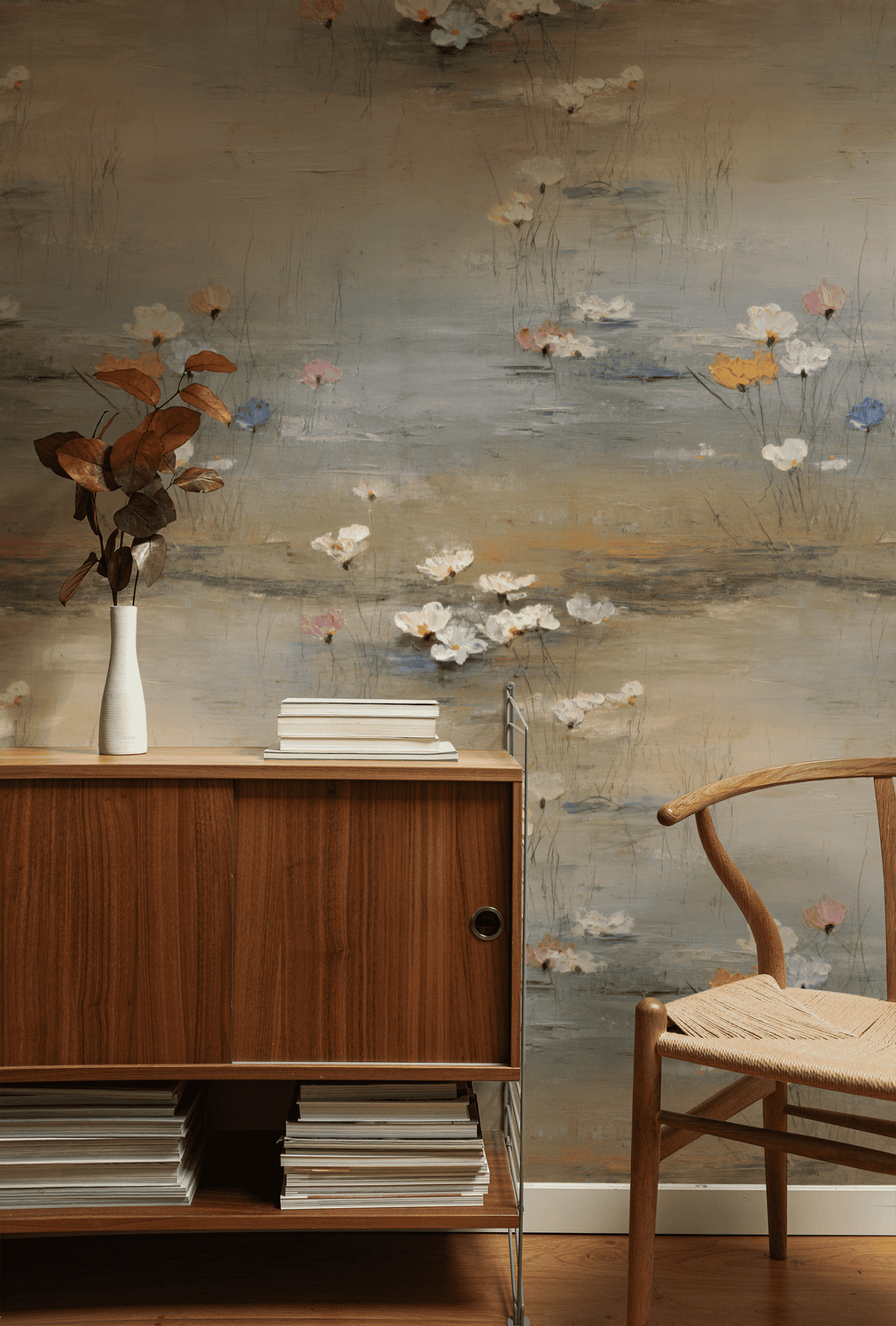 A mid-century wood cabinet and chair sit beside a vase with brown leaves, set against Serene Meadow Wallpaper with pastel flowers, creating a calming atmosphere in the room.