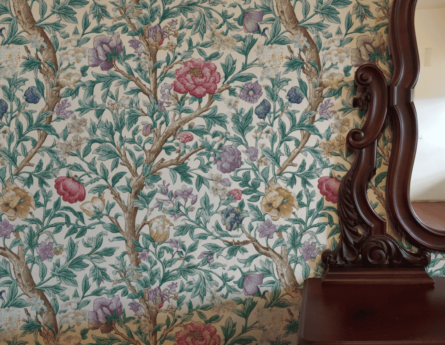Eden Blossom Wallpaper, featuring green leaves and colorful flowers, is partially reflected in a dark wooden mirror atop a matching dresser.