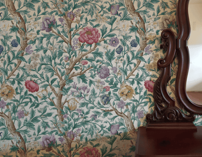 Eden Blossom Wallpaper, featuring green leaves and colorful flowers, is partially reflected in a dark wooden mirror atop a matching dresser.