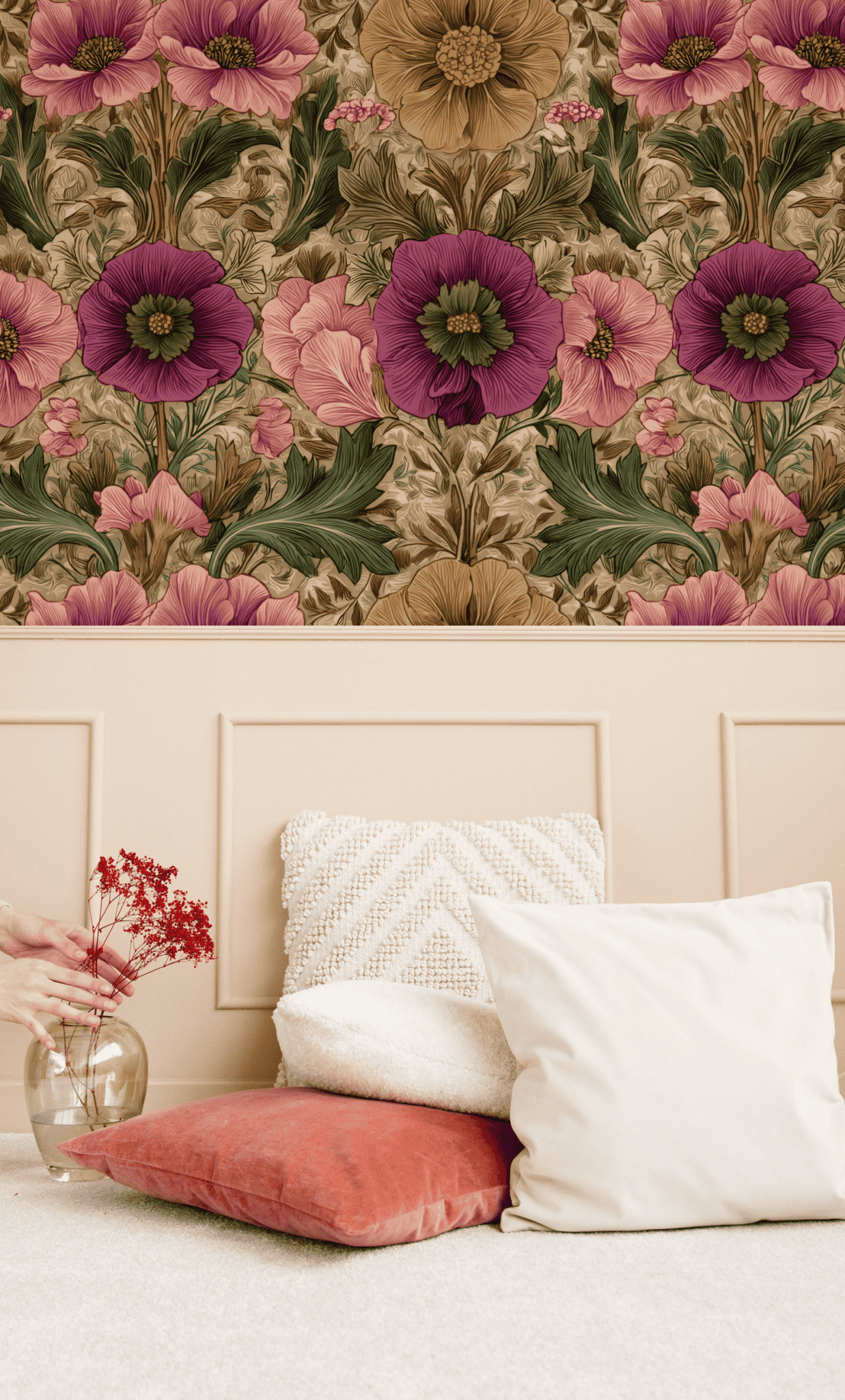 A beige wall covered with Vintage Flora Wallpaper featuring intricate floral designs above a headboard, paired with two white cushions, one rust cushion, and a glass vase with red flowers on a light carpet.