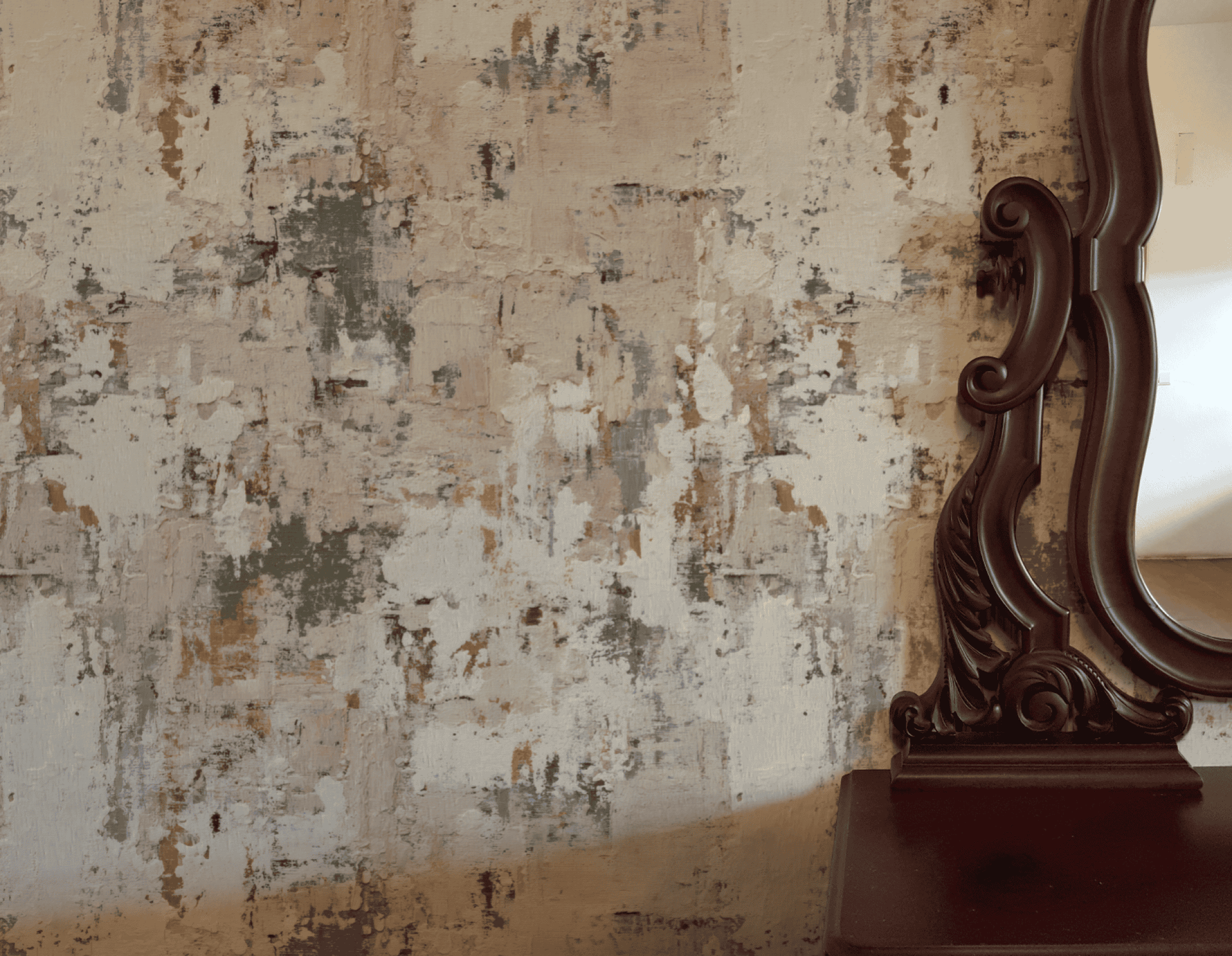 A decorative wooden mirror stands beside a wall adorned with Blush Palette Wallpaper, featuring textured abstract patterns in beige, gray, white, and muted green tones.