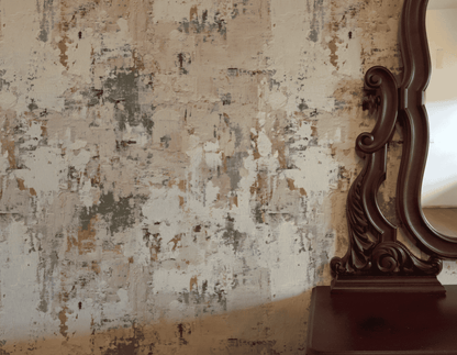 A decorative wooden mirror stands beside a wall adorned with Blush Palette Wallpaper, featuring textured abstract patterns in beige, gray, white, and muted green tones.