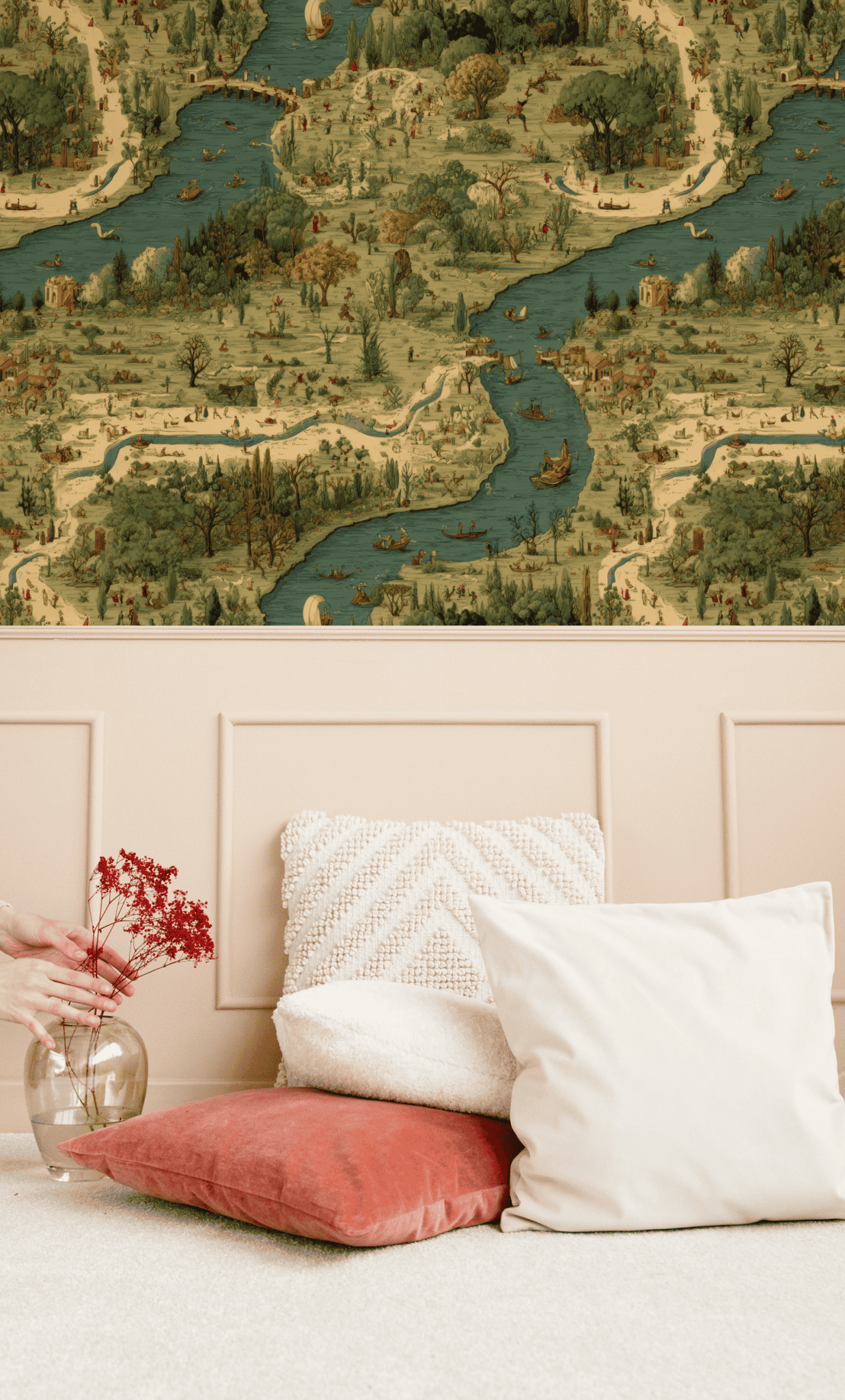 A beige wall adorned with the Pastoral Journey Wallpaper depicting rivers and villages hovers above a cushioned bench. On the floor, cushions and a glass jar with red dried flowers create a charming pastoral scene.