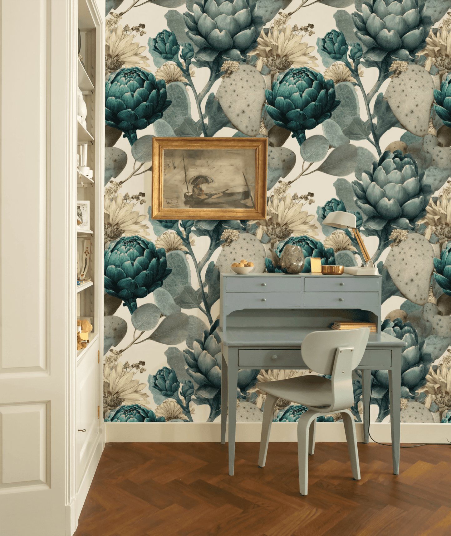 A small blue desk and chair are set against a wall adorned with Botanical Elegance Wallpaper; a framed painting hangs above the desk, and shelves are visible on the left.