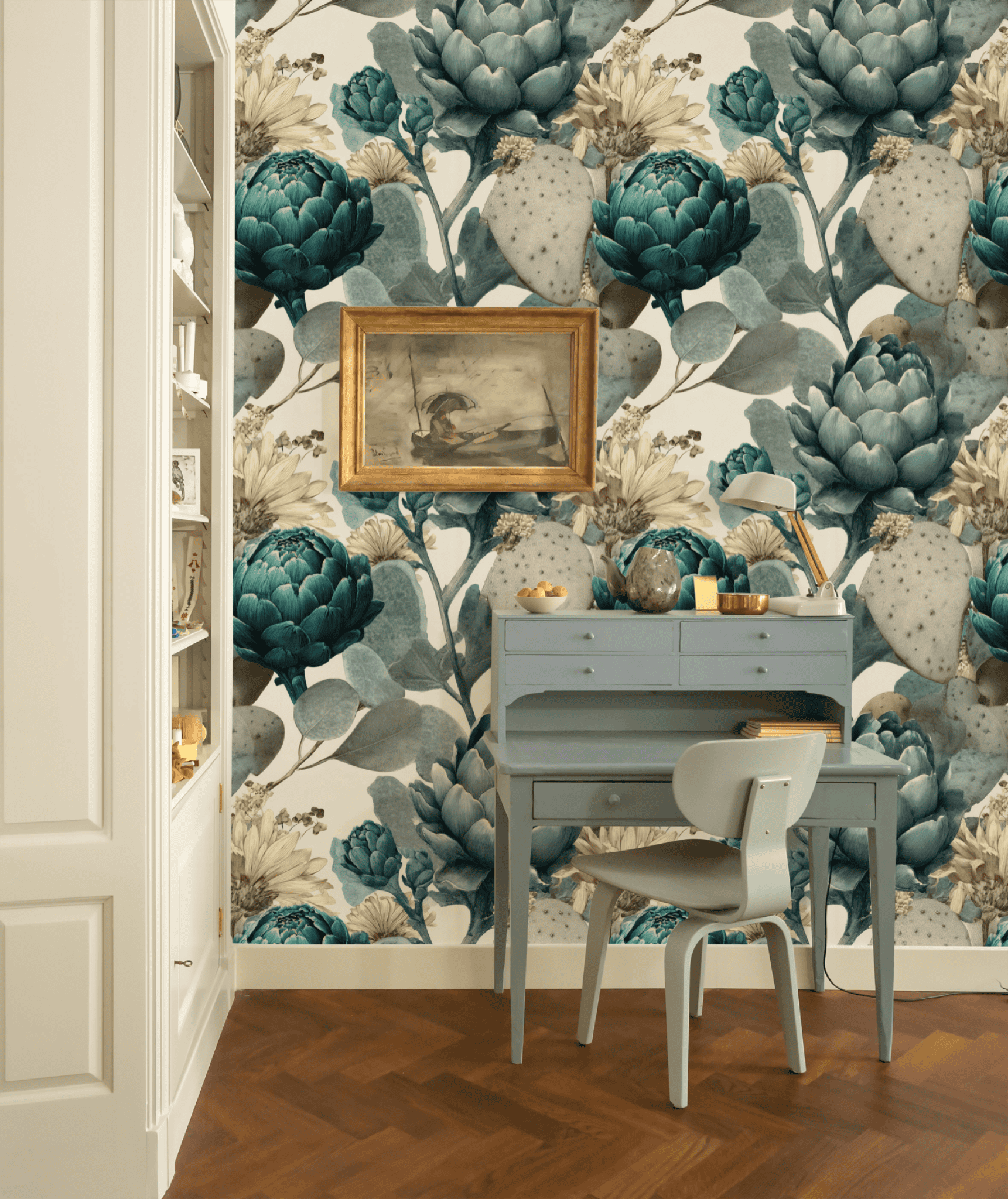 A small blue desk and chair are set against a wall adorned with Botanical Elegance Wallpaper; a framed painting hangs above the desk, and shelves are visible on the left.