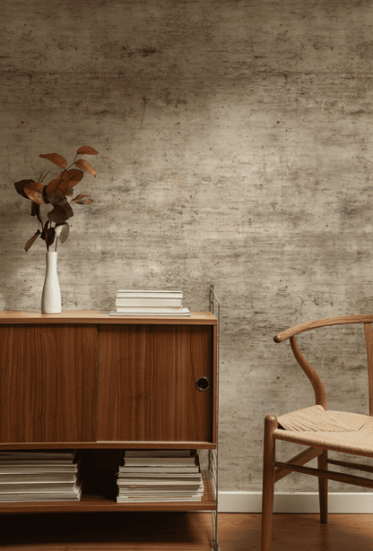 A wooden cabinet with books and a white vase of brown leaves sits by a wooden chair against Rustic Canvas Wallpaper, its earthy tones creating a cozy ambiance.