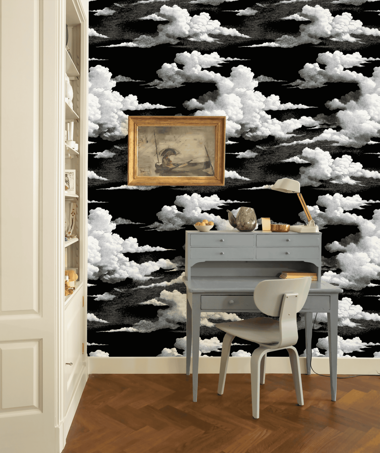 A small gray desk with a chair sits against a wall covered in Midnight Clouds Wallpaper. A framed painting hangs above the desk, and shelves to the left enhance the room’s celestial appeal.