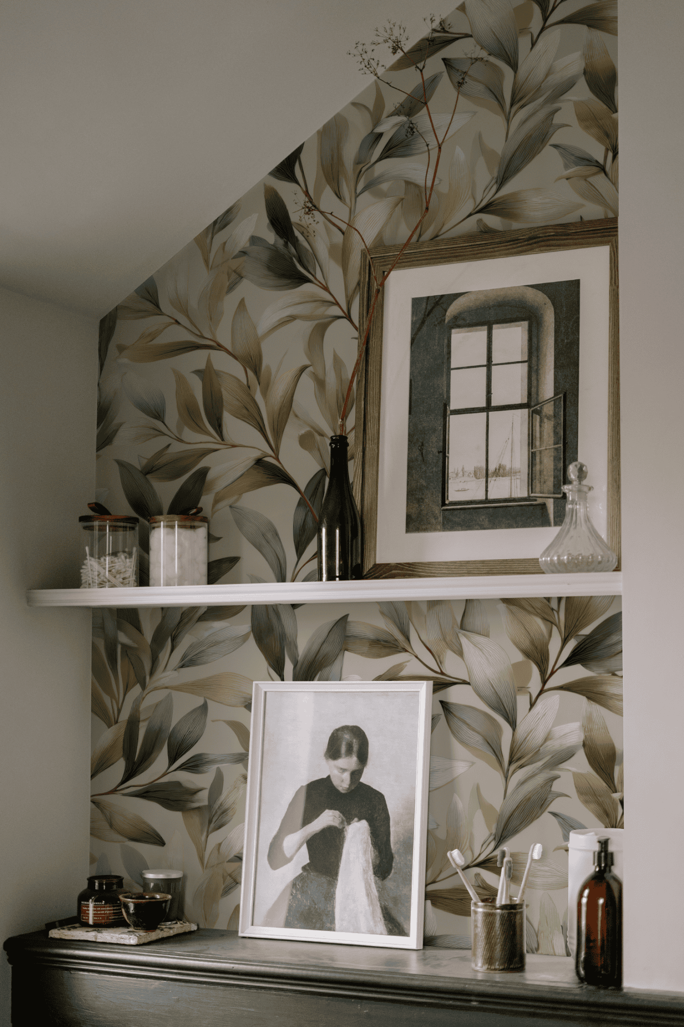 A shelf with jars, bottles, a decanter, and framed art sits against Verdant Elegance Wallpaper in soft greens, creating a natural, botanical ambiance.