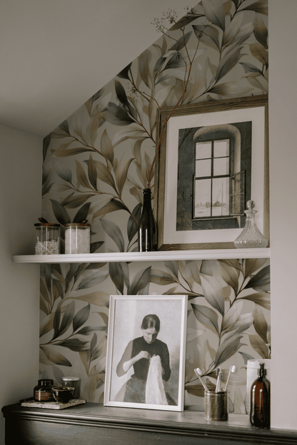 A shelf with jars, bottles, a decanter, and framed art sits against Verdant Elegance Wallpaper in soft greens, creating a natural, botanical ambiance.