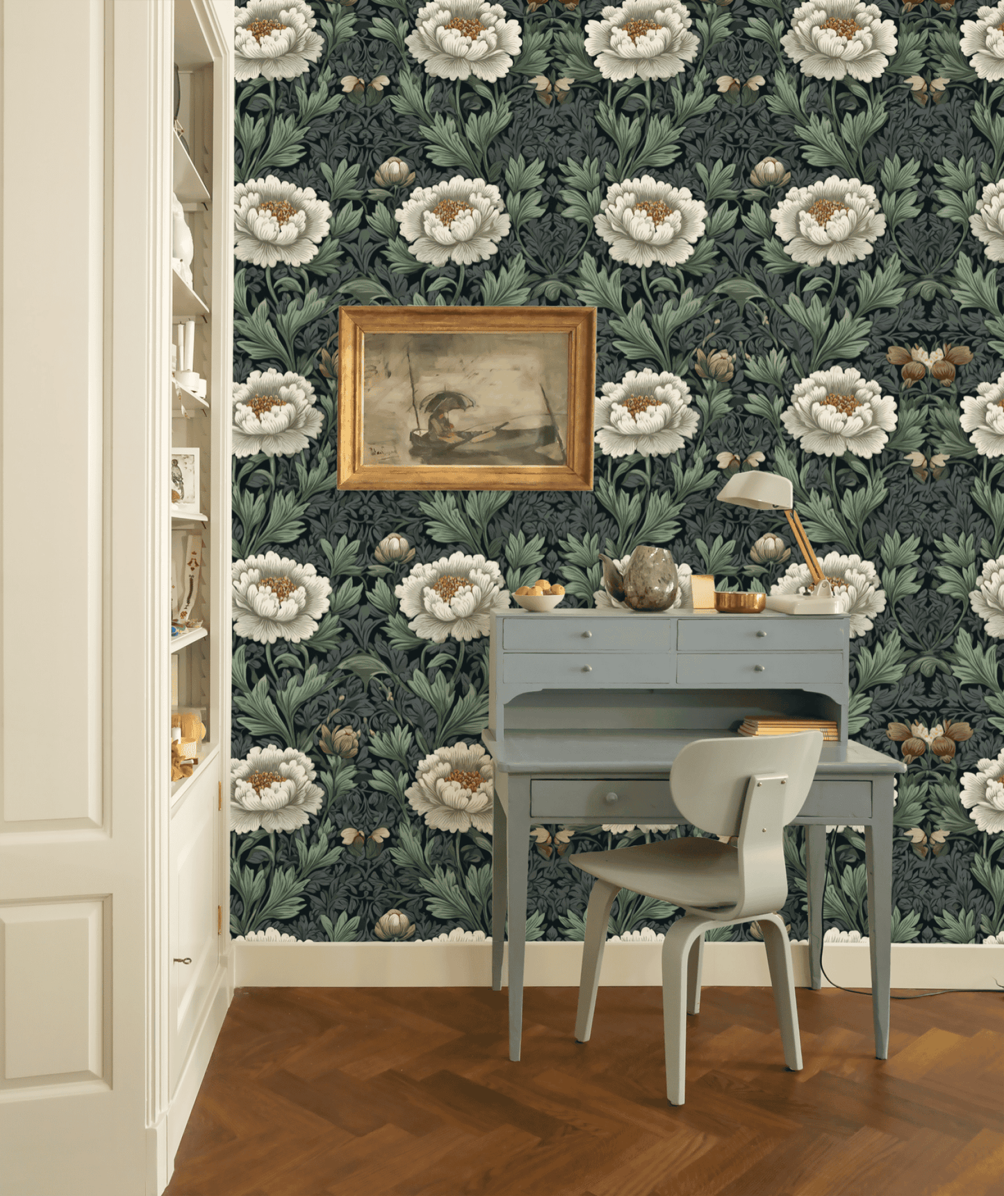 A small blue desk and chair sit against a wall covered in Serene Blooms Wallpaper with green leaves, a framed painting above, and a built-in bookshelf to the left, creating an elegant ambiance.