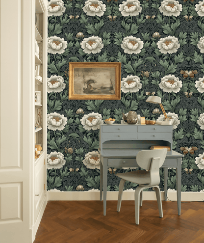 A small blue desk and chair sit against a wall covered in Serene Blooms Wallpaper with green leaves, a framed painting above, and a built-in bookshelf to the left, creating an elegant ambiance.