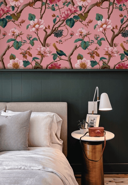 A bed with white and gray bedding sits beside a round nightstand with a white lamp, set against a wall decorated with Floral Serenity Wallpaper and dark green paneling.