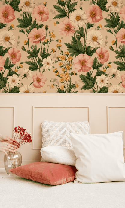 A hand arranges florals in a glass vase beside two throw pillows, set against soft peach and cream Blossom Reverie Wallpaper and beige wall panels.