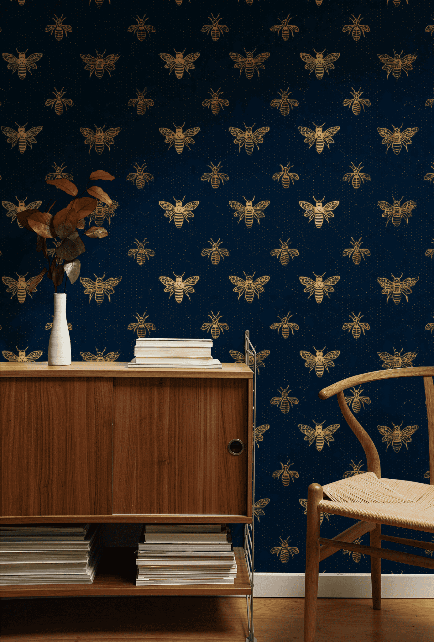 A wooden cabinet and chair sit against a dark blue wall covered in Golden Hive Wallpaper; a white vase with dried branches rests on the cabinet.