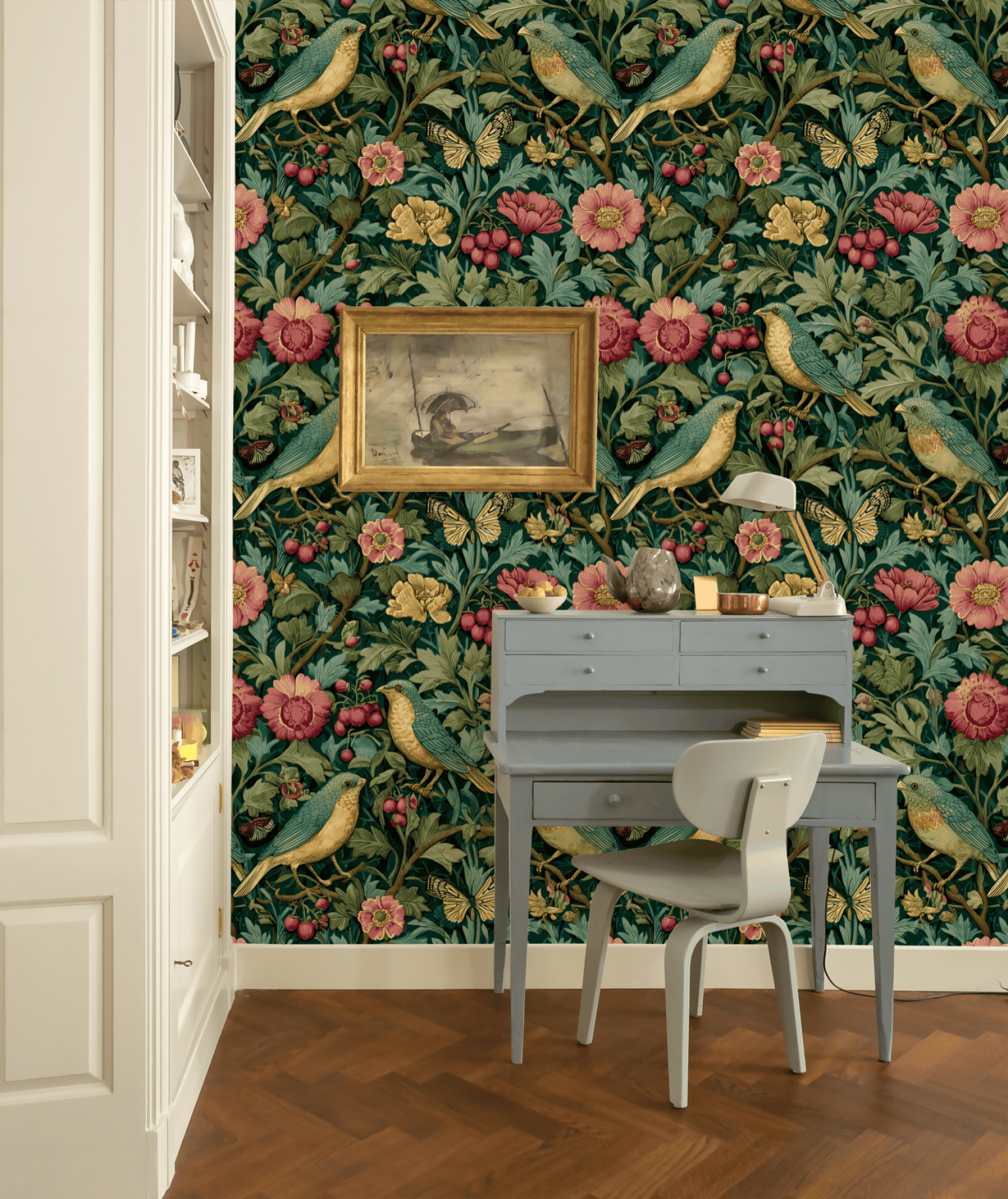 A small blue writing desk and chair are set against a wall decorated with Eden Blossom Wallpaper; a framed bird painting hangs above the desk.