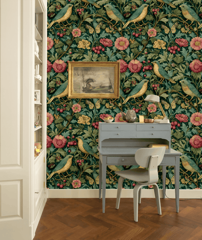 A small blue writing desk and chair are set against a wall decorated with Eden Blossom Wallpaper; a framed bird painting hangs above the desk.