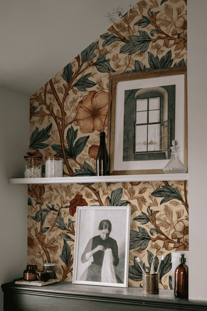 A shelf set against Botanical Harmony Wallpaper with vibrant blossoms displays glass jars, bottles, and framed art, featuring a photo of a woman and a painting of a window.