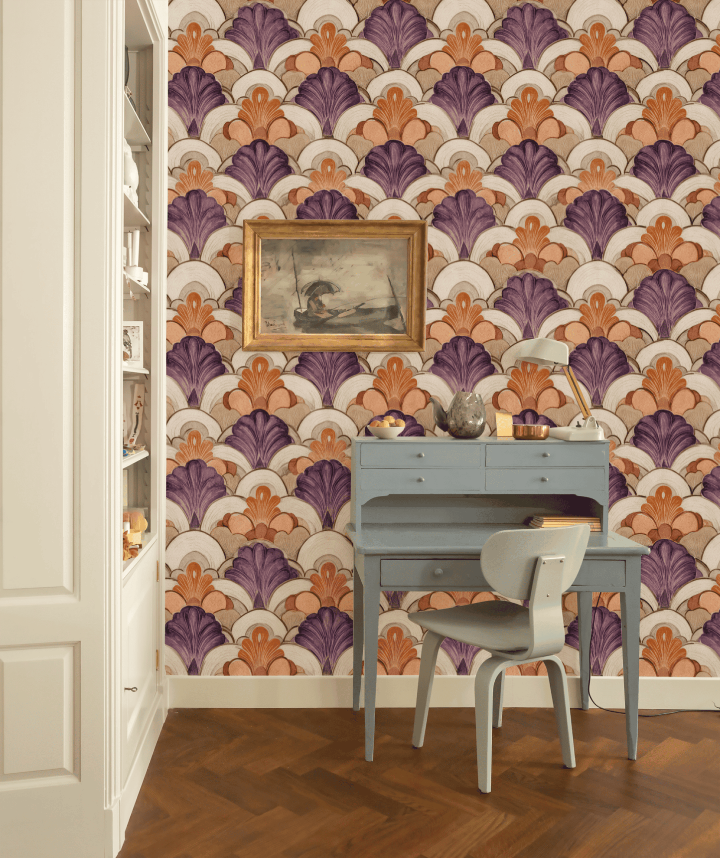 A small blue desk and chair sit in front of Deco Bloom Wallpaper, featuring colorful Art Deco fan patterns in purple and orange with floral accents; a framed painting hangs above the desk.