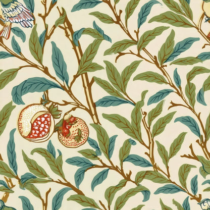 Slender green and teal leaves, split pomegranates and small birds wind across a warm cream ground, a William Morris design.