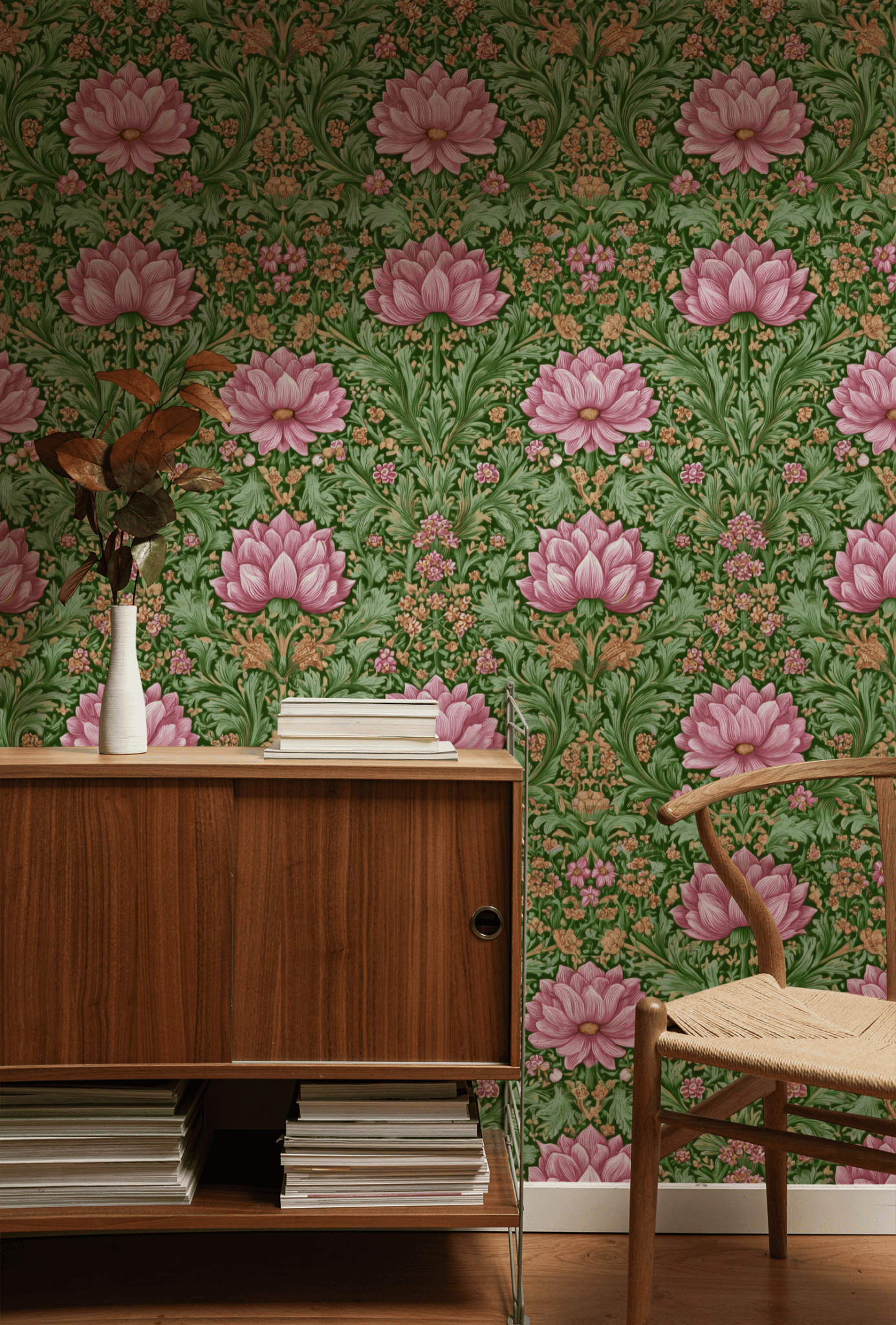 A wooden cabinet and chair sit against a wall covered with Bloom Harmony Wallpaper; a white vase with leaves and stacked books rest on the cabinet.