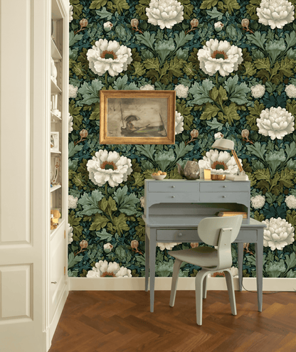 A small blue desk with a chair sits against a wall covered in Petal Bloom Wallpaper, beneath a framed painting and next to built-in shelves in a room with herringbone wood flooring.