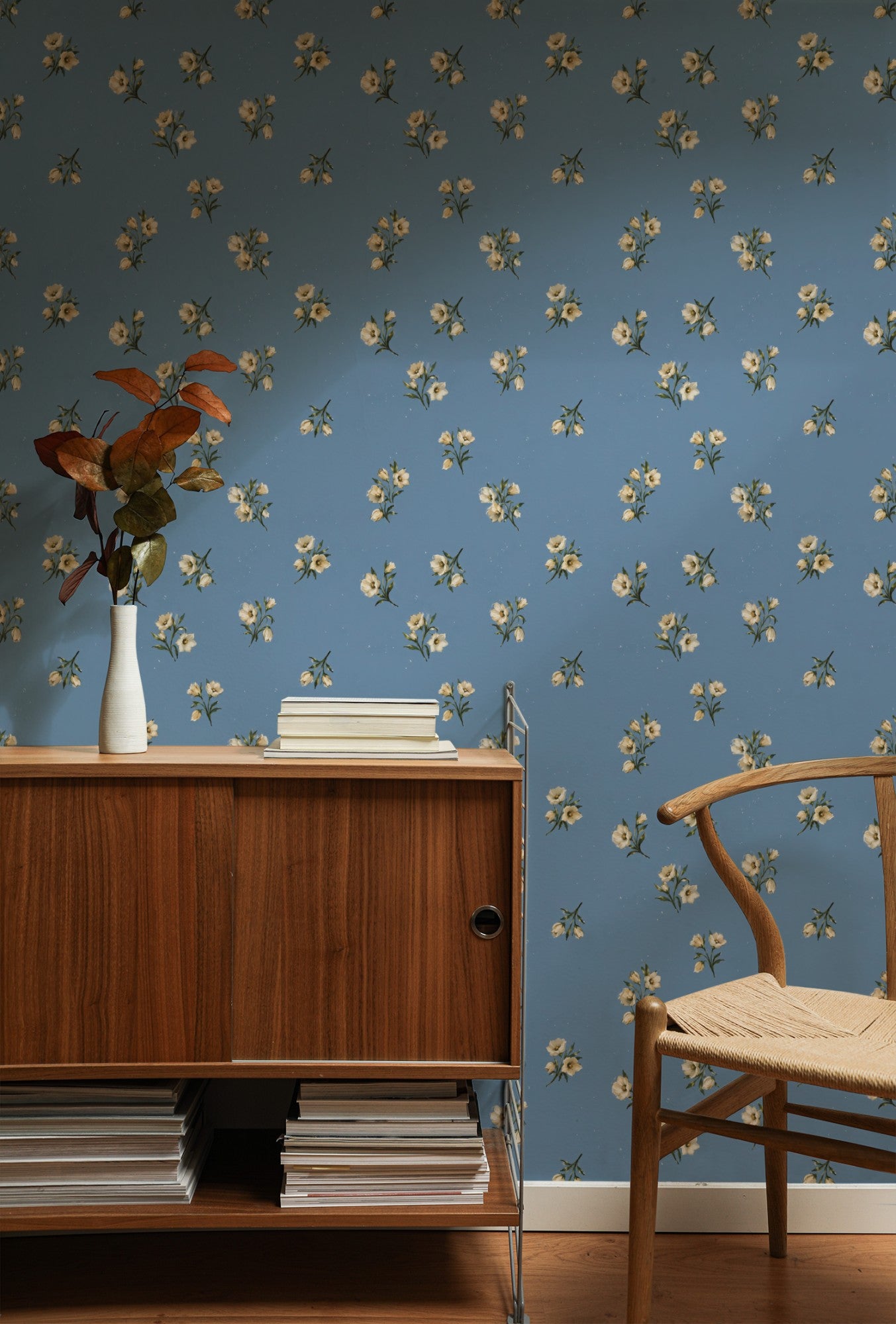 Cream wildflower sprigs scattered across a soft dusty-blue ground in a delicate painterly ditsy wallpaper.